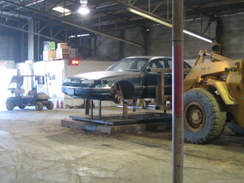 1985 Ford Crown Victoria LTD - A green sedan is elevated on a lift inside a garage, with a golf cart and a loader visible.