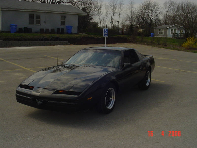 Black Pontiac Firebird parked in a lot. It has pop-up headlights and a distinctive front grille