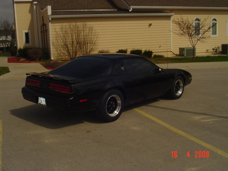 Black Pontiac Firebird with a rear spoiler and aftermarket wheels, parked on asphalt