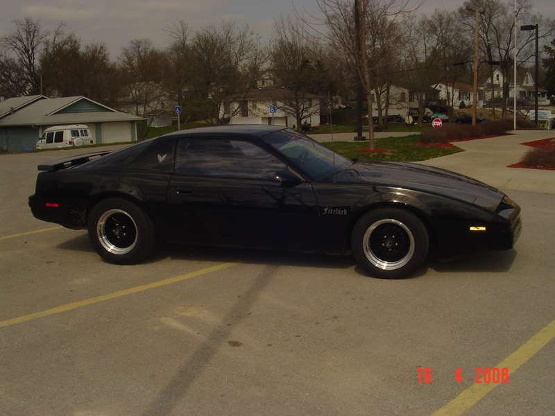 Black Pontiac Firebird coupe side profile in parking lot with black wheels