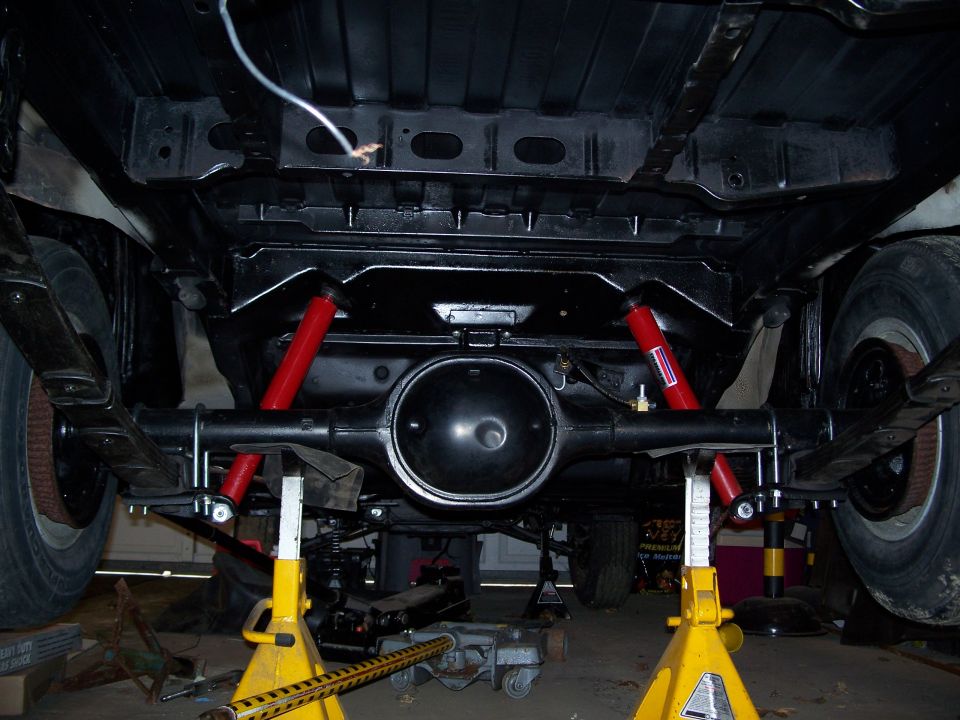 Underside view of a vehicle's rear axle, leaf springs, and red shock absorbers. It's on jack stands