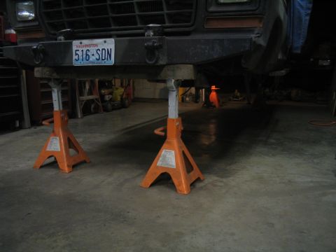 1979 Ford Bronco - A 1979 Ford Bronco is elevated on orange jack stands in a garage, showing its front bumper and license plate.