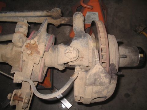1979 Ford Bronco - Close-up of a vehicle's front axle and brake system, showing suspension components and a brake caliper.