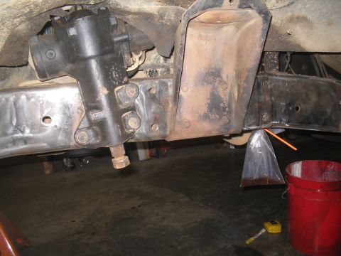 1979 Ford Bronco - Close-up view of a vehicle's steering system components, including the gear box and frame, with fluid collection in progress.
