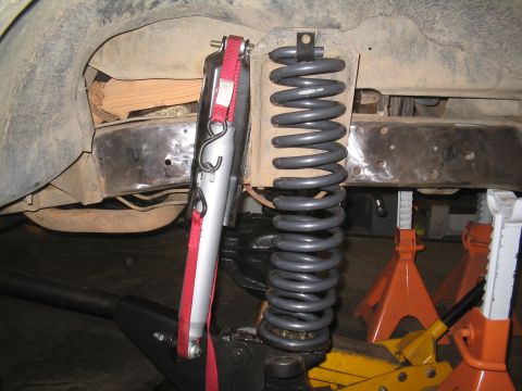 1979 Ford Bronco - Close-up of vehicle suspension components, including a coil spring and shock absorber, being worked on.