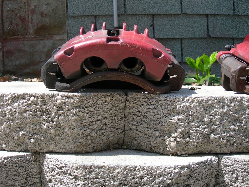 Red brake caliper with two pistons, resting on concrete blocks