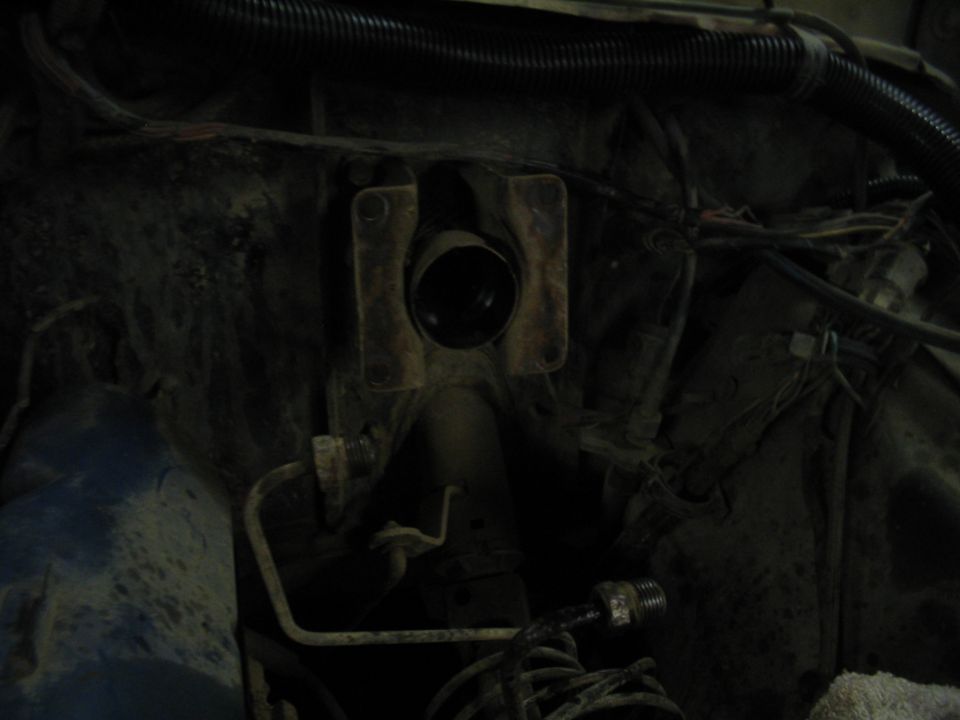 Engine bay with hoses and wiring, showing a metal bracket with a circular opening