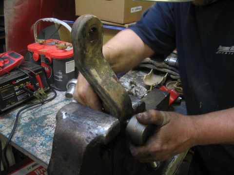 1979 Ford Bronco - A close-up of a mechanic's hands working on a metal component secured in a vise.