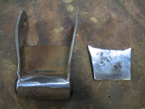 1979 Ford Bronco - Two metal parts, possibly for a vehicle suspension system, lie on a workbench.