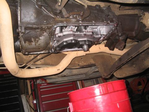 1979 Ford Bronco - The transmission pan has been removed, and fluid is draining into a red bucket during maintenance.