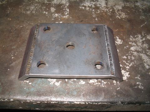 1979 Ford Bronco - A fabricated metal plate with multiple holes and welded edges rests on a textured surface.