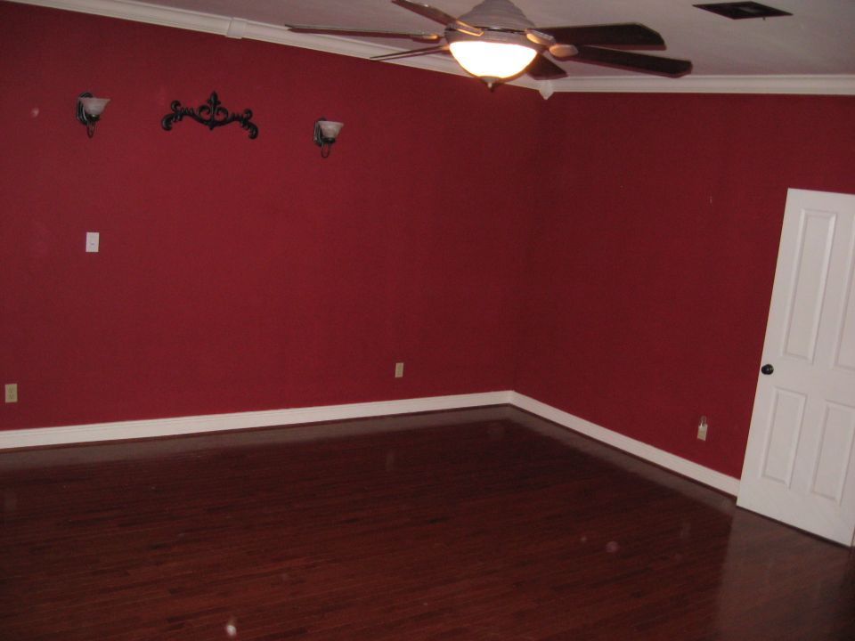 Interior scene with red walls, dark wood floor, ceiling fan, and white door