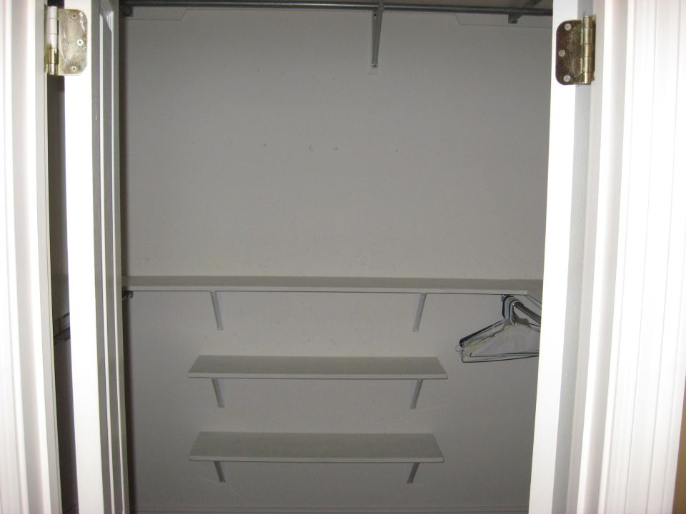 Interior of a white closet with a metal rod and three shelves. A single empty hanger is visible