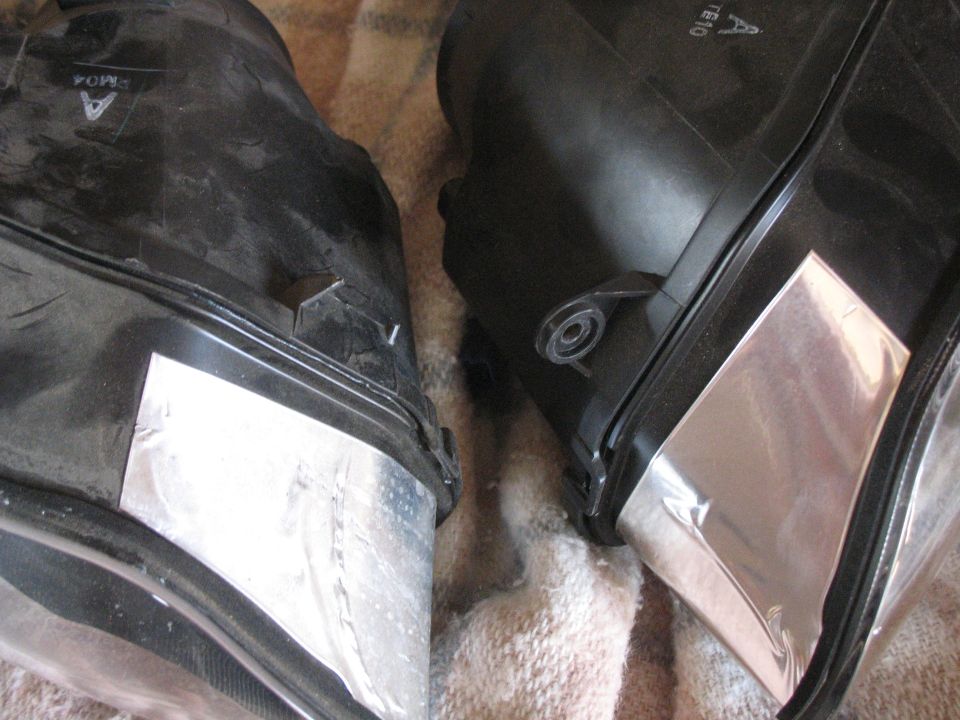 Two black plastic lamp housings with foil patches on a plaid blanket