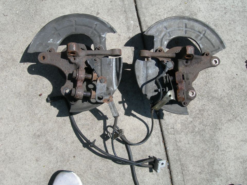 Pair of front wheel hub and brake assemblies with ABS sensors, laid out on concrete