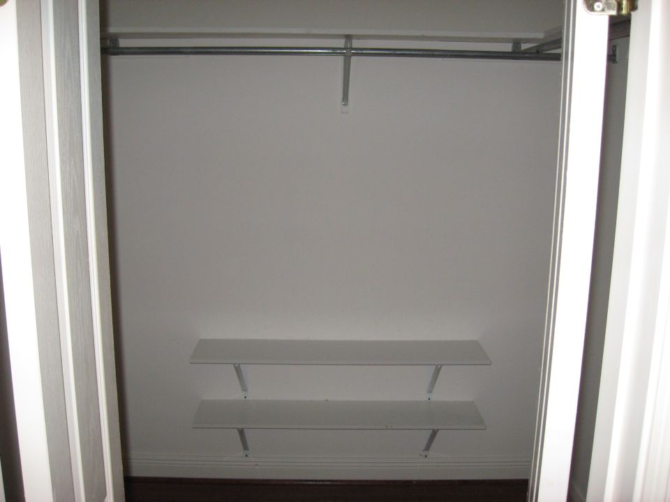 Empty white closet interior with a metal hanging rod and a small shelf