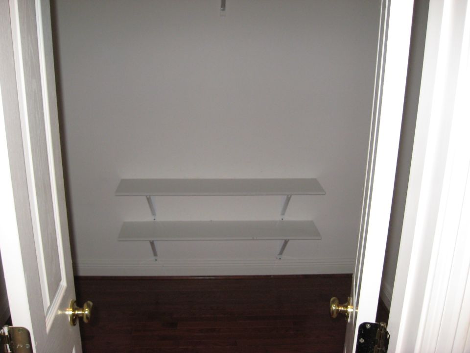 Empty closet interior with two white shelves and dark wood floor