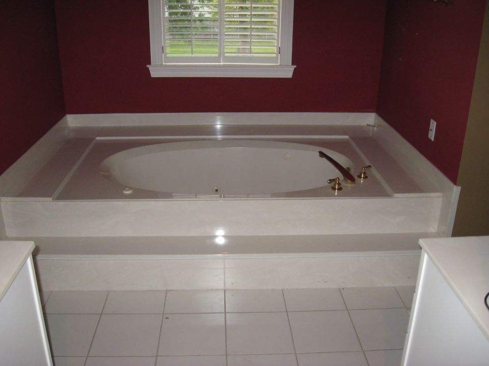 Bathroom with a large built-in bathtub, brass fixtures, and a window with white shutters