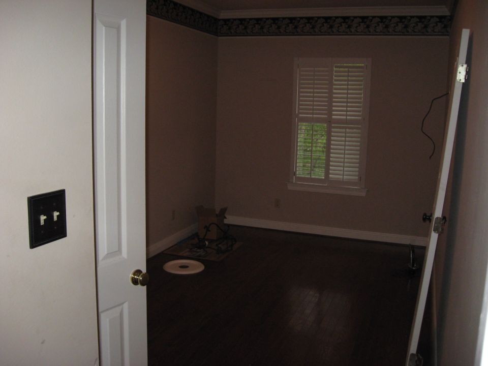 Interior room with dark wood floor, beige walls, a window with white shutters, and a partially open door
