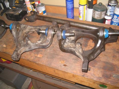 1979 Ford Bronco - Vehicle suspension components, including steering knuckles and a driveshaft, are laid out on a wooden surface.