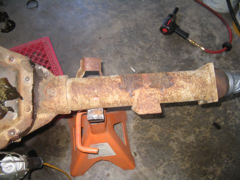 1979 Ford Bronco - A heavily rusted axle housing is supported by an orange jack stand in a garage setting.