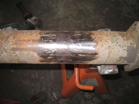 1979 Ford Bronco - Metal pipe being worked on with an angle grinder, supported by jack stands.