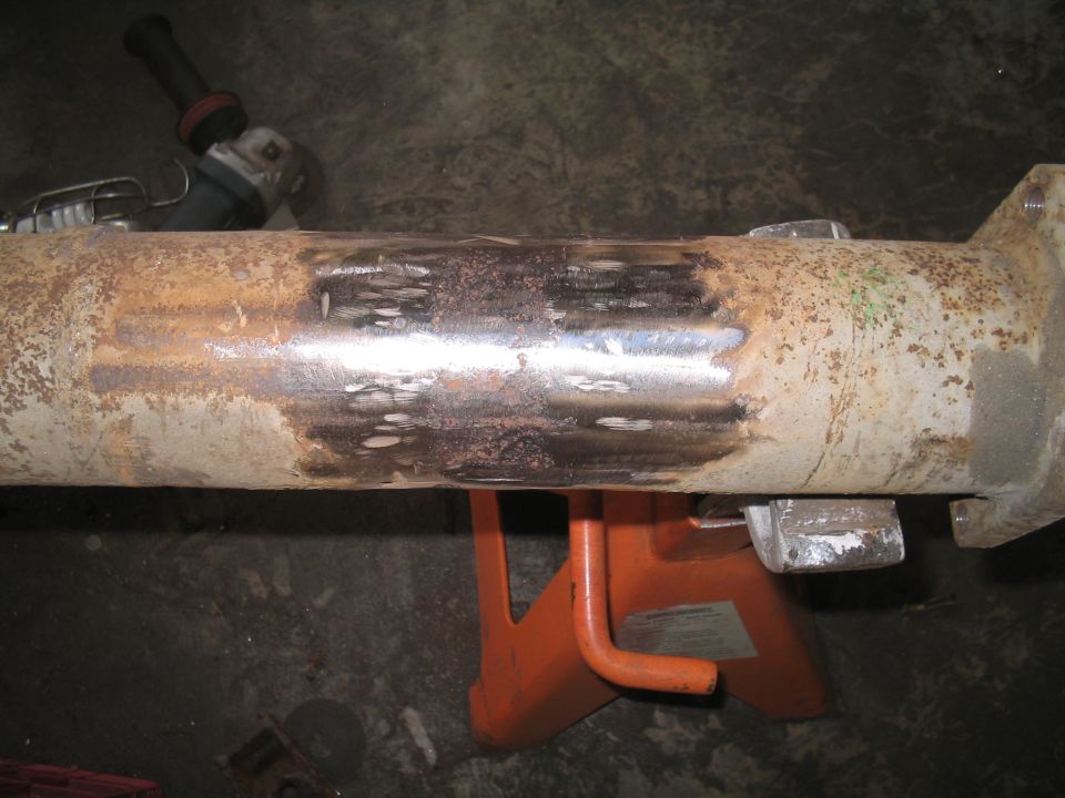 Rusty metal pipe section on orange jack stands, with an angle grinder in the background