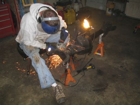 1979 Ford Bronco - A person grinds an axle assembly supported by jack stands in a garage.