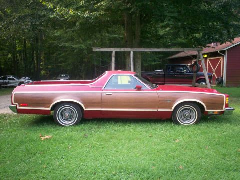 1973 Ford Ranchero - A red and wood-paneled pickup truck is parked on a grassy lawn next to a red barn.