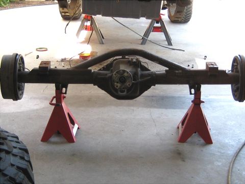 1996 Ford Bronco - The rear axle assembly of a vehicle is supported by red jack stands in a garage.