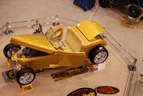 1996 Ford Bronco - A gold custom hot rod roadster is displayed with its hood and doors open, revealing its tan interior and chrome accents.