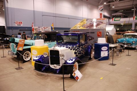 1996 Ford Bronco - A model kit box for a 1940 Ford Sedan is displayed alongside several vintage vehicles at an indoor event.