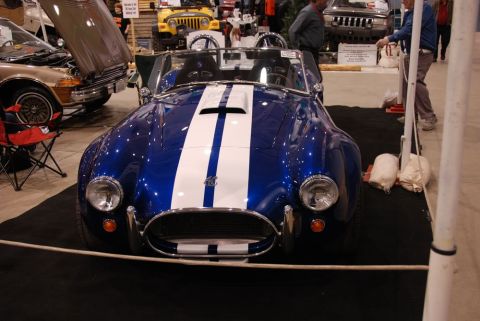 1996 Ford Bronco - Blue and white AC Cobra replica on display at an indoor event with other vehicles present.