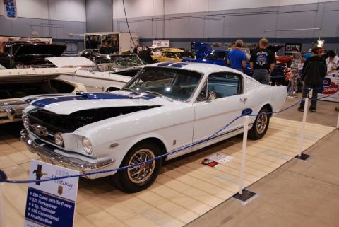 1996 Ford Bronco - White 1966 Ford Mustang with blue racing stripes on display at an indoor car show.