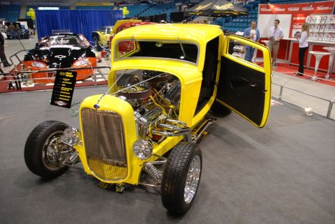1996 Ford Bronco - Yellow hot rod on display indoors, showing its engine and custom build.