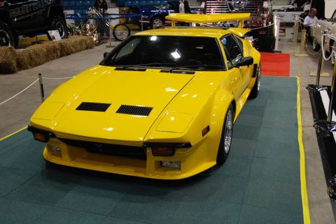 1996 Ford Bronco - A bright yellow sports car with a prominent rear wing is displayed indoors, with other vehicles and exhibits visible in the background.