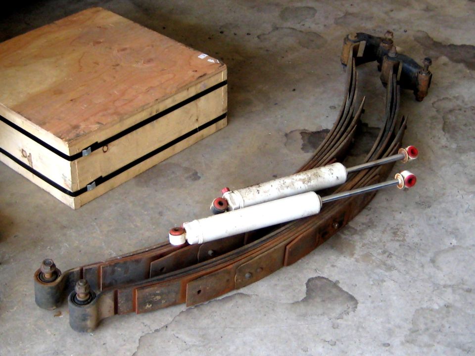 Leaf springs and shock absorbers on concrete floor next to wooden crate