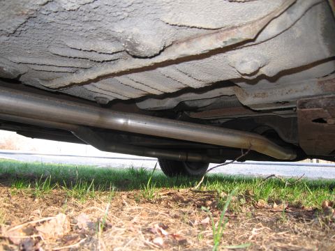 1991 Ford LTD Crown Victoria - The underside of a vehicle reveals its exhaust pipes and frame, with grass and dirt visible below.