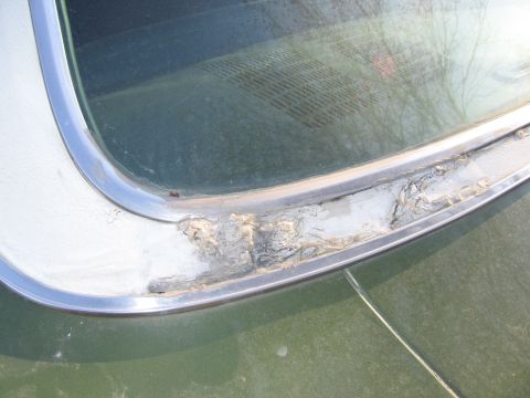 1991 Ford LTD Crown Victoria - The chrome trim around the rear window of a vehicle is heavily corroded and peeling.