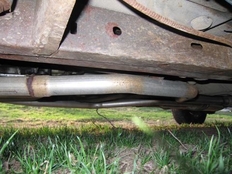 1991 Ford LTD Crown Victoria - The rusted undercarriage and exhaust pipes of a vehicle are visible, with grass in the foreground.