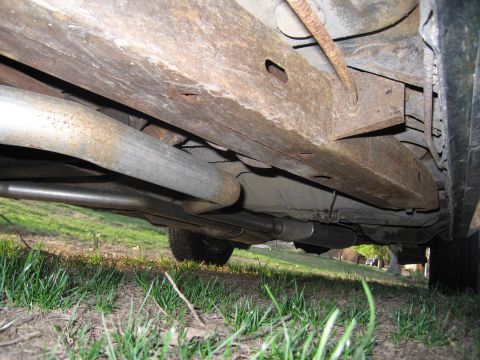 1991 Ford LTD Crown Victoria - The underside of a vehicle displays significant rust on its frame and exhaust system.