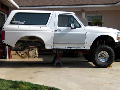 1996 Ford Bronco - A white SUV is elevated on jack stands, revealing its undercarriage and suspension components.