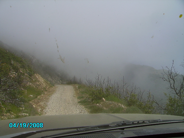 View from inside a vehicle driving on a foggy gravel road up a mountainside