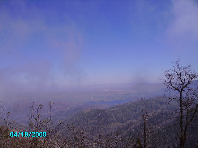 Misty mountain landscape with bare trees in the foreground and a blue sky
