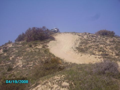 1990 Ford Bronco - A vehicle navigates a steep, sandy incline under a clear blue sky.
