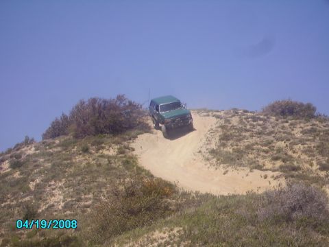1990 Ford Bronco - A green SUV navigates a steep dirt incline under a clear blue sky.