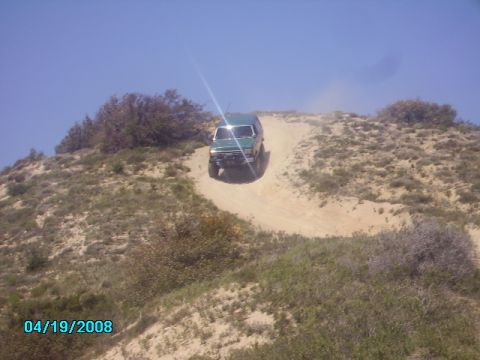 1990 Ford Bronco - A green 1990 Ford Bronco navigates a dusty incline on a clear day.