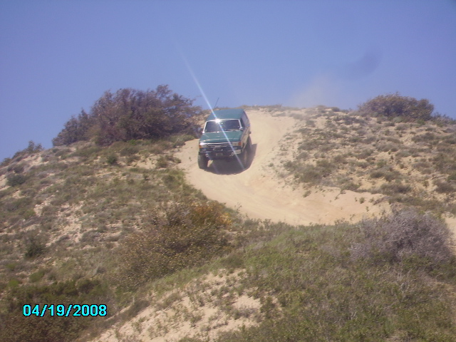 Green 1990 Ford Bronco driving up a dirt hill