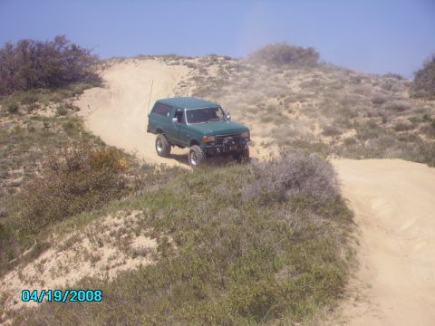 1990 Ford Bronco - A 1990 Ford Bronco navigates a dusty, off-road trail on a sunny day.