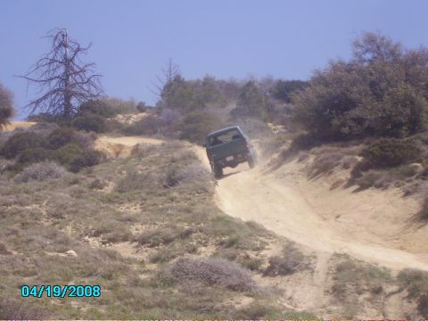 1990 Ford Bronco - A green SUV navigates a steep, dusty trail under a clear blue sky.
